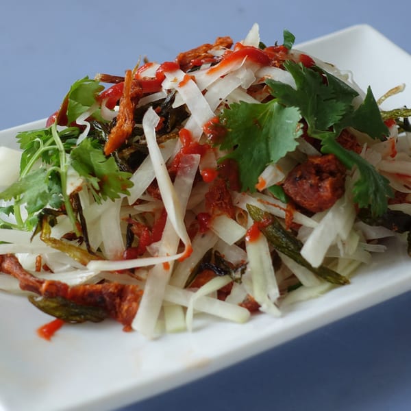 Close-up of a Vietnamese salad with shredded daikon, herbs, and red chili sauce on a white plate.