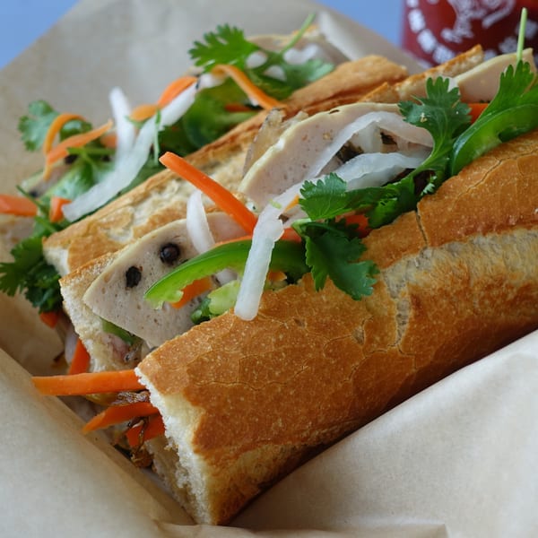 Two O Banh Mi sandwiches, filled with meat, pickled carrots, daikon, cilantro, and jalapeños.