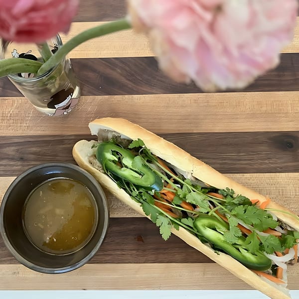O Banh Mi's banh mi sandwich with jalapeños, cilantro, and carrots, next to a bowl of broth.